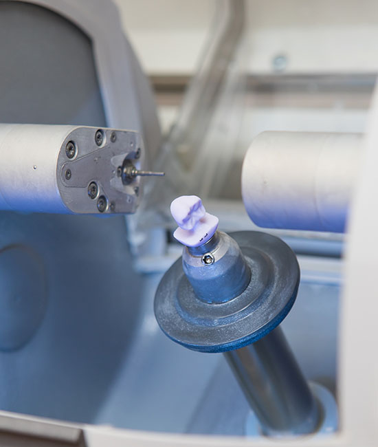 The image shows a close-up view of an industrial 3D printer with a partially completed object on the print bed, and there s a small pink object being printed.